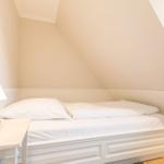 Ein Bett unter Dachschrägen mit weißer Bettwäsche und Nachttisch.