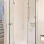 Duschkabine mit Glaswand und Toilettenpapierhalter. Treppenhaus im Hintergrund.