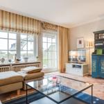 Wohnzimmer mit Sofa, Glas-Tisch und Fernseher. Fenster mit Jalousien und Blick auf Außenbereich.