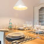 Esszimmer mit gedecktem Tisch, weißen Stühlen und Glasvitrine.