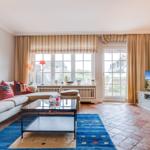 Wohnzimmer mit Sofa, Couchtisch und TV. Große Fenster mit Blick nach draußen.