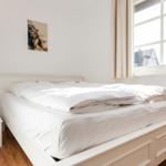 Schlafzimmer mit weißem Bett, Fenster und Stehlampe.