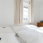 Schlafzimmer mit Doppelbett, Fenster und Holzschrank.