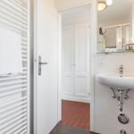 Badezimmer mit Waschbecken, Spiegel und Handtuchhalter. Durchgang zur Garderobe mit rotem Boden.