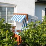 Blau-weiße Strandkörbe stehen im Garten vor einem weißen Haus.