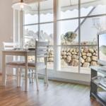 Essbereich mit Tisch, Stühlen und Fernseher. Große Fenster mit Blick auf Steinmauer und Garten.