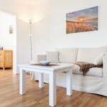 Wohnzimmer mit Sofa, Tisch und Wandbild. Holzfußboden und weiße Wände.