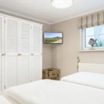 Bedroom with white bed, wardrobe, and TV on the wall.