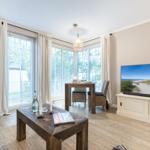 Living and dining area with large windows, TV, and wooden table.