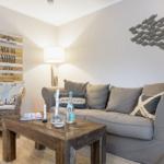 Living room with sofa, armchair, and wooden table. Wall decor with fish motif and wooden sign.