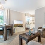Living room with dining table, TV, and kitchen area. Wooden furniture and wall decor.