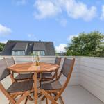 Terrasse mit Holztisch und vier Stühlen. Im Hintergrund sind Häuser und Bäume zu sehen.