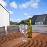 Terrasse mit Tisch, Stühlen und Weinglas. Hintergrund: Haus und Himmel.