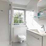 Badezimmer mit Dusche, Waschbecken und Toilette. Fenster mit Blick auf Grün.