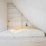 Schlafzimmer mit Dachschrägen, Bett und Regalwand.
