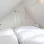Schlafzimmer mit Doppelbett, weißer Wand und Tür unter Dachschrägen.