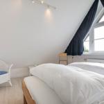 Schlafzimmer mit Doppelbett, weißen Wänden und großem Fenster mit dunkelblauen Vorhängen.