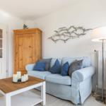 Wohnzimmer mit Sofa, Holzschrank und Stehlampe.