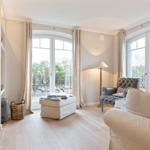 Wohnzimmer mit Sofa, Sessel und großem Fenster zum Garten.