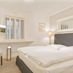 Schlafzimmer mit Bett, Fernseher und Fenster mit Jalousien.