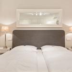 Schlafzimmer mit Doppelbett, zwei Nachttischen und Lampen. Spiegel über dem Bett.