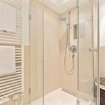 Dusche mit Glaswand, Handbrause und Heizkörper mit Handtüchern.