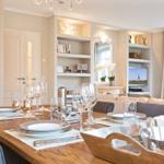 Esstisch mit Geschirr und Gläsern im Essbereich mit Wohnzimmer im Hintergrund.