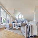 Living room with sofa, armchair, and balcony. Wooden floor and sloped ceiling.