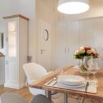Dining area with wooden table, white chairs, and flower vase.