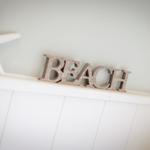 Wooden sign reading BEACH and two white starfish on a white panel wall.