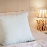 A bed with pillows and a bedside lamp with a wooden base.