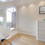 A bedroom with a white chair, dresser, and TV on the wall. Balcony with view of outdoor area.