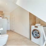 Bathroom with washing machine and toilet under sloped ceiling