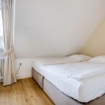 Schlafzimmer mit Doppelbett, Holzboden und Fenster mit Vorhang.