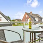 Terrasse mit Tisch, zwei Stühlen und Weinflasche. Blick auf Häuser und Grünflächen.