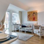 Wohn- und Essbereich mit nautischem Sofa, Glas-Tisch und Fenster zum Balkon.