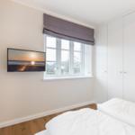 Schlafzimmer mit Bett, Fenster und TV an der Wand.