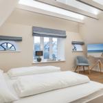 Schlafzimmer mit Dachschrägen, großem Bett und Fenstern mit Blick nach außen.