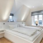 Schlafzimmer mit Doppelbett, Fenster und TV. Holzboden und weiße Wände.