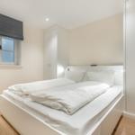 Schlafzimmer mit weißem Bett, Kleiderschrank und Fenster mit Rollladen.