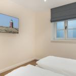 Schlafzimmer mit Bett, Fenster und Wandbild eines Leuchtturms.