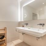 Badezimmer mit Waschbecken, Spiegel und Holzregal mit Handtüchern.