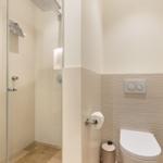 Dusche mit Glaswand, Toilette und Toilettenpapierhalter.