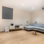 Wohnzimmer mit grauem Sofa, Holzboden und Projektionssystem.