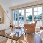 Living room with glass table, sofa, and armchair. Large window front with balcony view.