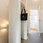 Hallway with clothes rack, wall lamp, and view into bathroom.