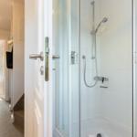 Shower cabin with glass enclosure and shower head. Door leads to living area with window.