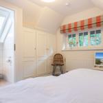 Bedroom with sloped ceiling, window, TV, and adjacent toilet.