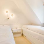 Two beds in an attic room with window and nightstand.