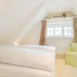 Double bedroom with sloped ceiling, window, and green seating.